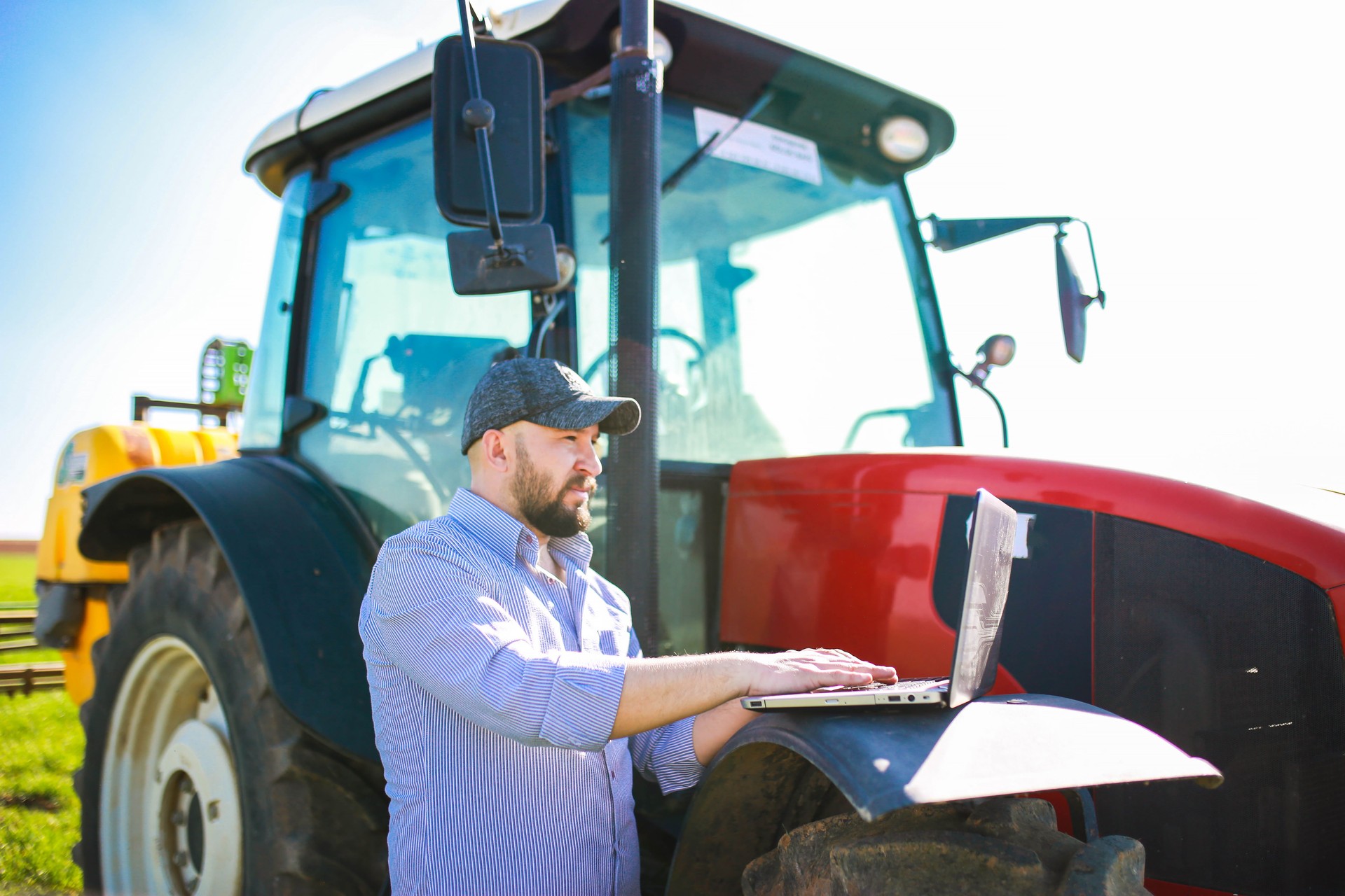 Jovem agrônomo usando aplicativo de agricultura inteligente com seu laptop na frente de seu trator no campo. conceito de agricultura inteligente